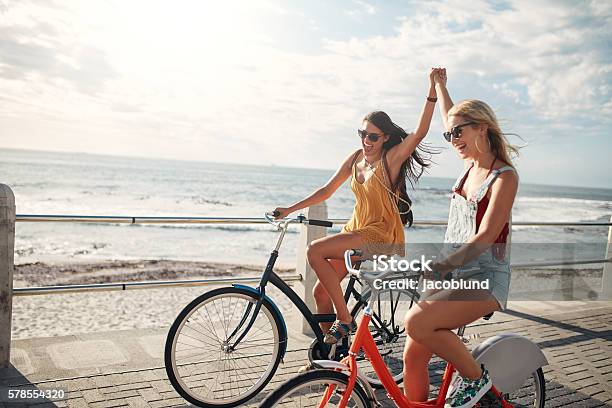 Female Friends Enjoying Cycling On A Summer Day Stock Photo - Download Image Now - Friendship, Beach, Cycling