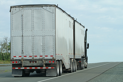 Rear quarter view of a semi tractor truck equipped with a double trailer, often called a B-train, hauling bulk cargo on an interstate highway.