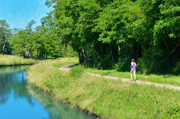 Active woman runner jogging near canal river, outdoors running, sport and healthy lifestyle concept