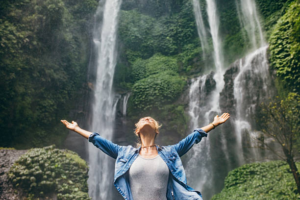 istock Young woman standing in front of waterfall 578557922