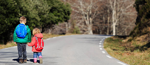 istock brother and sister with backpacks walking on the road 578565430