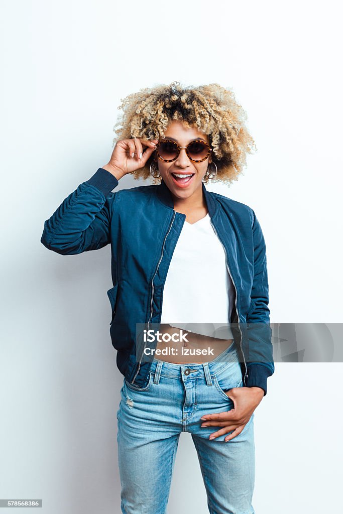 Portrait of cool afro american young woman Portrait of sensual afro american young woman wearing bomber jacket, denim trausers and sunglasses, laughing at camera.  Sunglasses Stock Photo