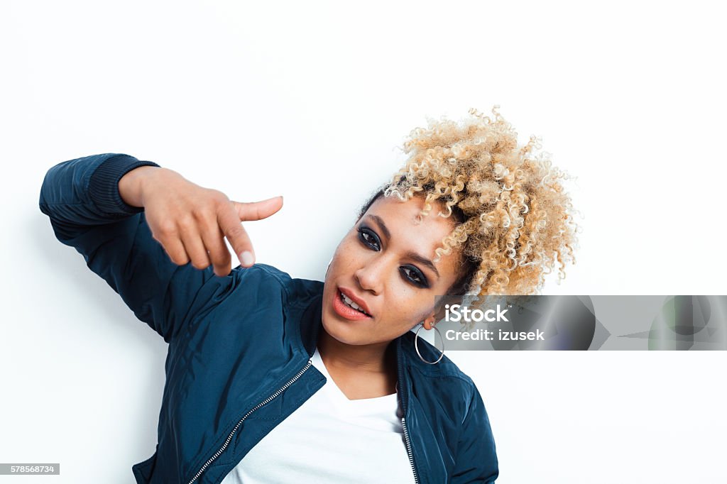 Portrait of cool afro american young woman Portrait of cool afro american young woman wearing bomber jacket, pointing at camera, standing against white background. Bomber Plane Stock Photo