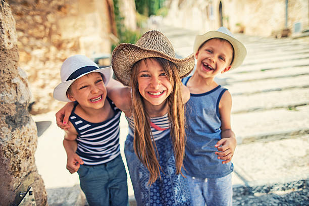 Kids having fun visiting the beautiful Majorcan town of Pollenca Sister and two brothers having fun visiting the beautiful Majorcan town of Pollenca. Kids are embracing and laughing to the camera. Behind them there are famous stairs of Pollenca. three amigos stock pictures, royalty-free photos & images