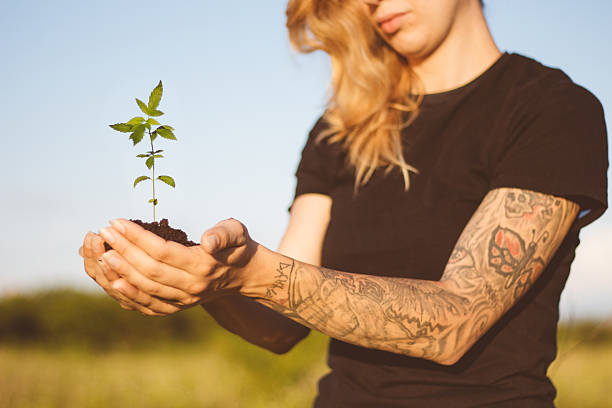 Marijuana plant in hands of young girl Profile portrait of young tattoed girl holding a cannabis flower marijuana tattoo stock pictures, royalty-free photos & images