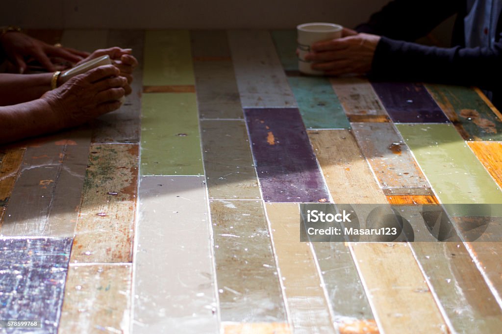 Three women sitting at a soft pastel colors' table There is a soft pastel colors' table. Three women are sitting around it. Two of them have coffee cups. Sun light shines a half of the table. Adult Stock Photo