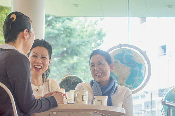 Three adult women chatting at a coffee shop Three women are sitting and chatting at a coffee shop in Tokyo. They all look happily with laughing. stay at home saying stock pictures, royalty-free photos & images