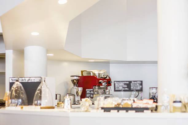 There are some of coffee equipments and glasswares in the counter of coffee shop. The counter table, walls, and pillars of the counter of this coffee shop has white color.