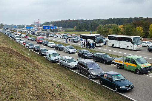 Stuttgart, Germany - October 17, 2015: Long line of vehicles waiting at State Highway at Stuttgart international airport after heavy  car crash; group of soccer fans standing in front of the bus, drinking beer at the highway