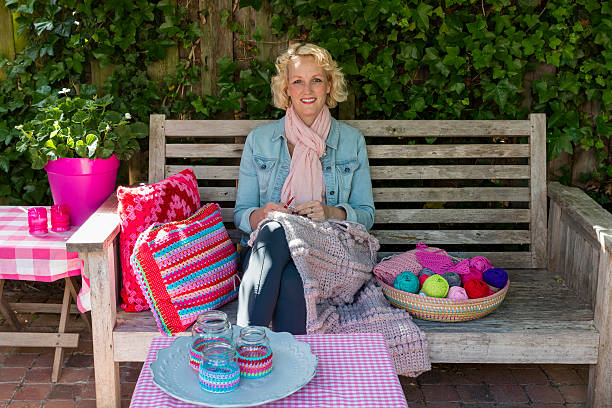 Smiling Young Blond Woman Crochets In The Garden stock photo