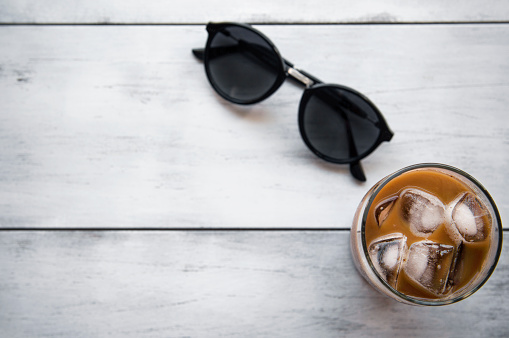 Ice coffee sunglasses on white wooden table.
