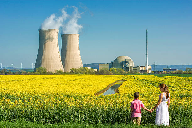 Mother Holding Hands with Son at Nuclear Power Station Rear view on Young mother holding hand of her son looking concerned at him in front of flowering canola field and nuclear power station. Some small wind turbines in the background on the left side of the two cooling towers. Useful as symbol for future and energy questions. nervous holding hands stock pictures, royalty-free photos & images