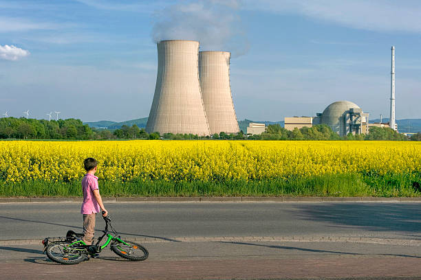 ragazzo con biciclette in campo di colza e centrale nucleare - nuclear power station nuclear energy child nuclear reactor foto e immagini stock