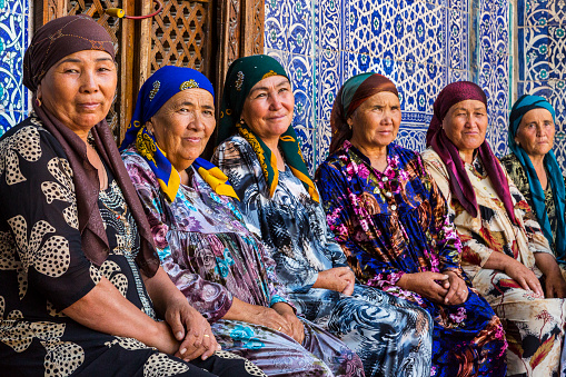 Khiva, Uzbekistan - May 23, 2016: Uzbek women in colorful dresses sit and rest as they look at me in Khiva, Uzbekistan.