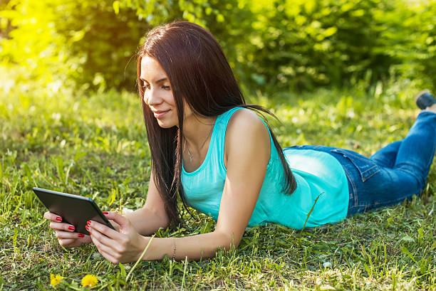 istock Young woman lying on the grass and using tablet 578804034