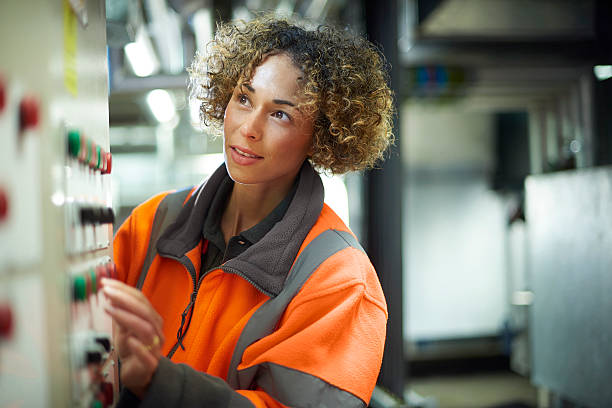 female maintenance engineer A female industrial service engineer conduct a safety check of a control panel and boiler room  . She is wearing hi vis and turning a dial on the control panel. heating engineer stock pictures, royalty-free photos & images