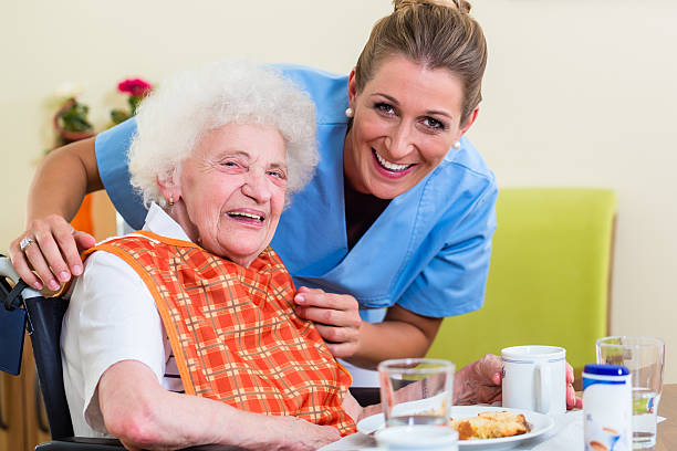nurse with senior woman helping with meal - senior adult nursing home eating home interior imagens e fotografias de stock