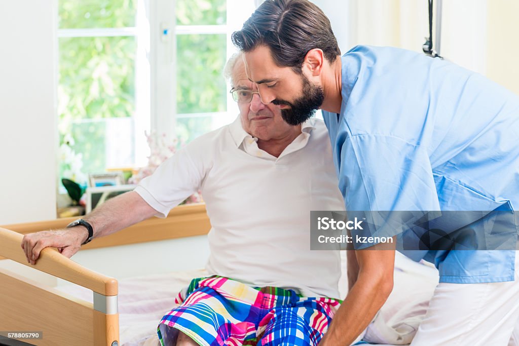 Elderly care nurse helping senior from wheel chair to bed Home Caregiver Stock Photo