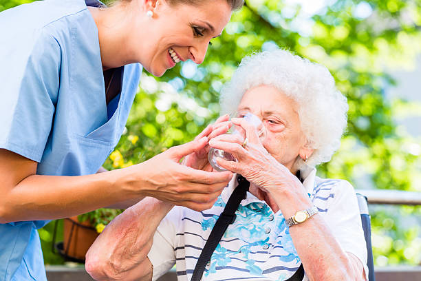 Geriatric nurse giving glass of water to senior woman stock photo