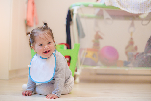 baby girl is smiling at camera , crawling and sitting in a playroom