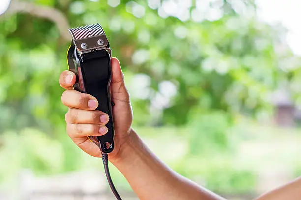 Man holding hair clippers on nature background.