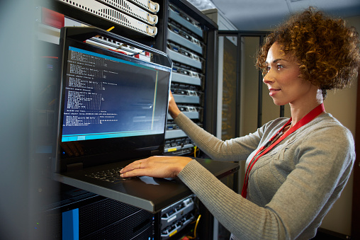 a female IT technician is editing the programme on the network server in a server room. ** all identifying script and racking has been modified **
