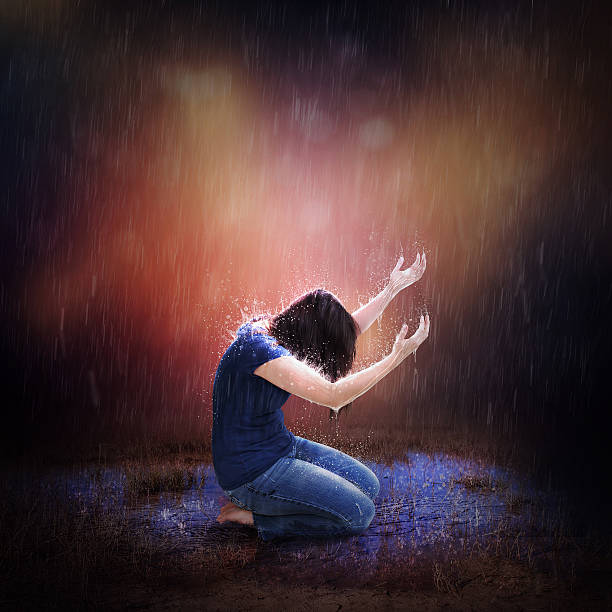 Rainstorm Prayer A woman kneeling to pray during a heavy rain storm. kneeling stock pictures, royalty-free photos & images