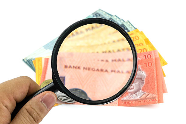 Magnifying glass looking at banknotes and coins on white background Hand holding magnifying glass looking at banknotes and coins on white background coins of ringgit of malaysia stock pictures, royalty-free photos & images