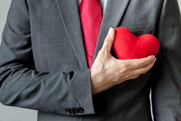 hombre de negocios mostrando compasión sosteniendo el corazón rojo en su pecho - imitation beauty beautiful looking at camera fotografías e imágenes de stock