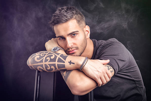 Handsome and stylish young man with black t-shirt. Cool tattoos on arms