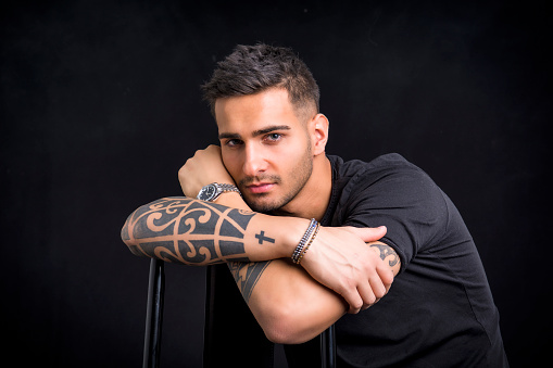 Handsome and stylish young man with black t-shirt. Cool tattoos on arms