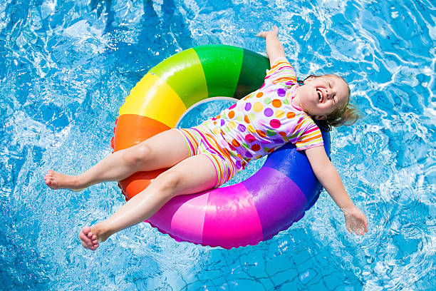 Child in swimming pool playing with colorful inflatable ring Happy little girl playing with colorful inflatable ring in outdoor swimming pool on hot summer day. Kids learn to swim. Children wearing sun protection rash guard relaxing in tropical resort swimming float stock pictures, royalty-free photos & images