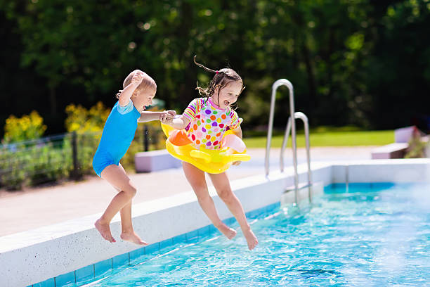 Happy little kids jumping into swimming pool Happy little girl and boy holding hands jumping into outdoor swimming pool in a tropical resort during family summer vacation. Kids learning to swim. Focus on boy. one piece swimsuit photos stock pictures, royalty-free photos & images