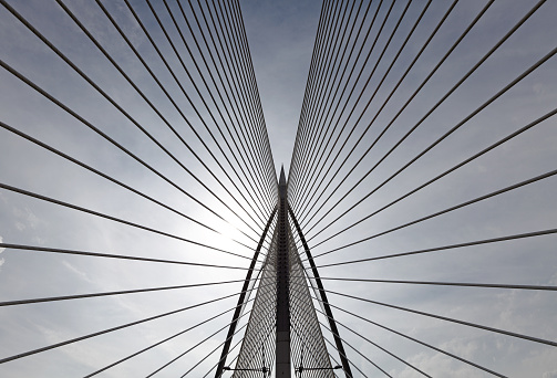 Abstract pattern of suspended cable lines silhouette against a blue cloudy sky.