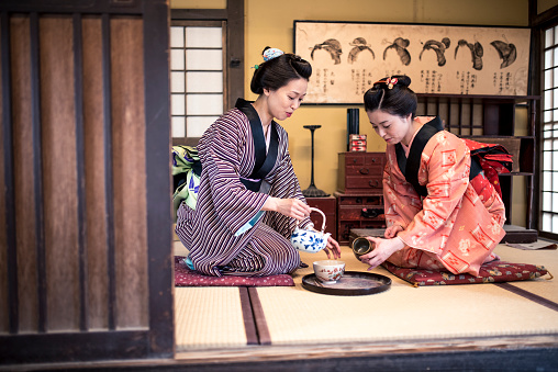 Two Japanese women wearing a kimono drinking tea indoors, in tea room. They are talking and having fun.