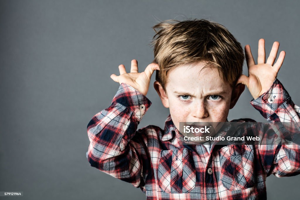 angry little brat enjoying making a grimace for misbehavior angry little brat enjoying making a grimace, sticking out his tongue, playing with his hands for  misbehavior, contrast effects, grey background Child Stock Photo