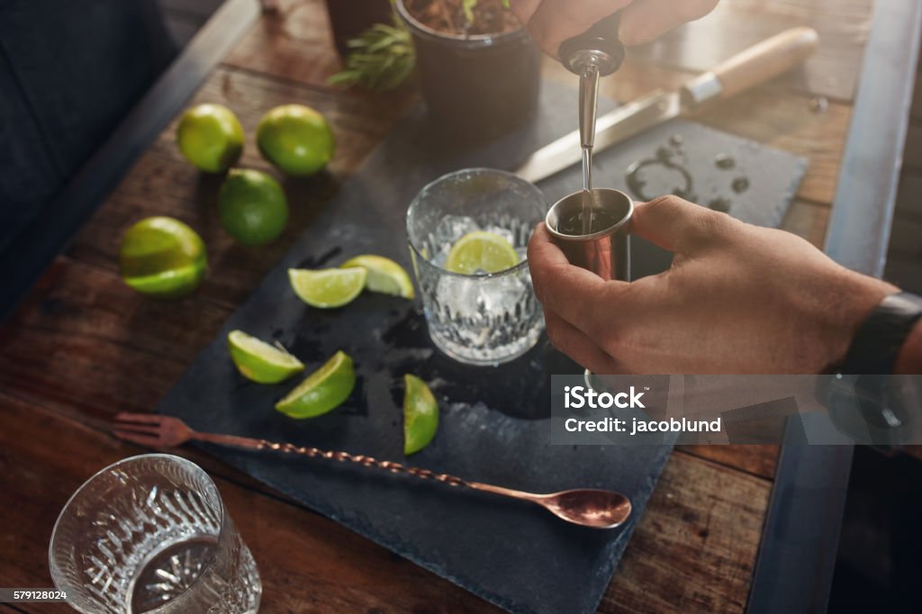 Pouring alcohol in jigger to prepare a cocktail Closeup of man hands pouring alcoholic drink in to a jigger to prepare a cocktail. Barman preparing the cocktail at  the bar counter. Cocktail Stock Photo