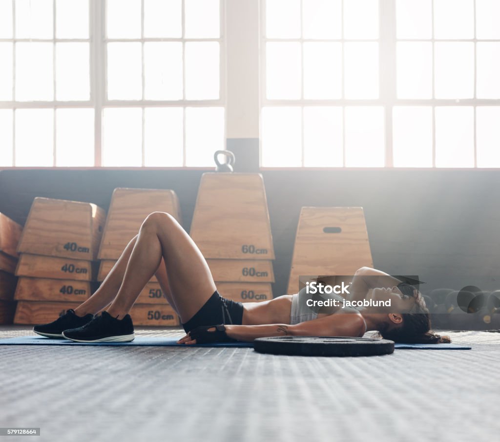 Fitness woman relaxing after exercise session Young woman lying on her back at the gym after her workout. Fitness woman relaxing after exercise session. Tired Stock Photo