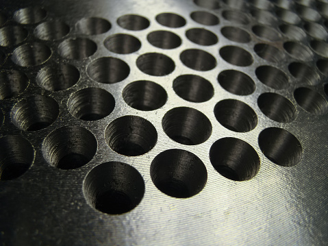 Many holes drilled in a shiny metal plate for matrix extruder detail.