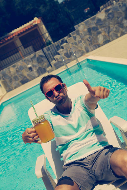 istock Young man on the pool holding jar with orange juice. 579136342