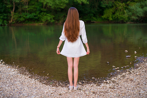 Rear view full length little girl standing in autumn park with lake outdoor, looking at sunset. From behind child model posing in fall forest. Childhood emotion concept. Copy text space for ad