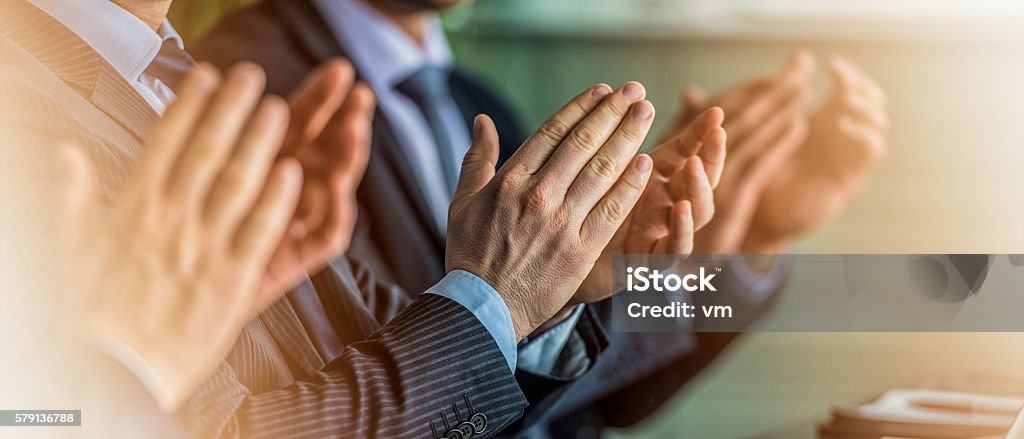 Close up of businessmen in suits clapping Close up panoramic shot of people in full suits sitting behind a table and clapping Applauding Stock Photo