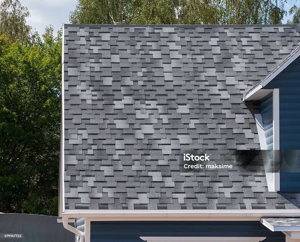 The roof with bitumen shingles The roof of the house lined with gray bitumen shingles Roof Tile Stock Photo