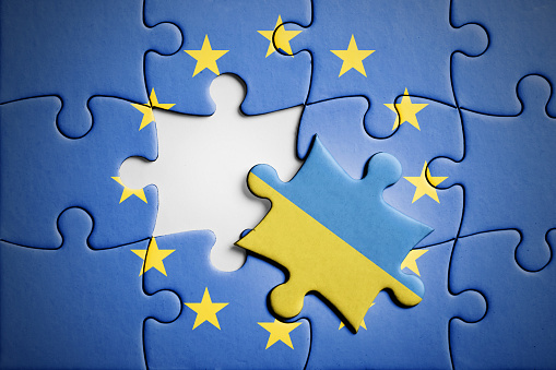 Political relations between Ukraine and European Union, concept puzzle. Flag of European Union on puzzle in background, with one blank place and one piece with flag of Ukraine in front. Studio shot. Horizontal orientation.