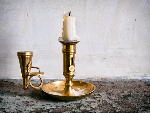 A used candle dripping with wax in an old Victorian brass candlestick standing on a distressed shelf.