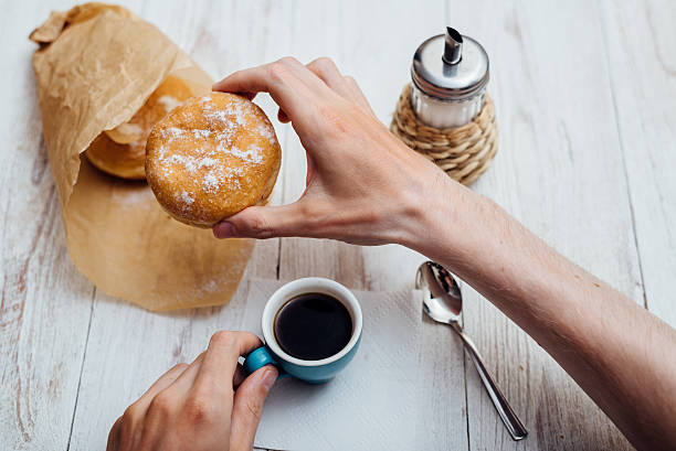istock Man hands eating Bismarck donut with coffee on wooden table 579221536