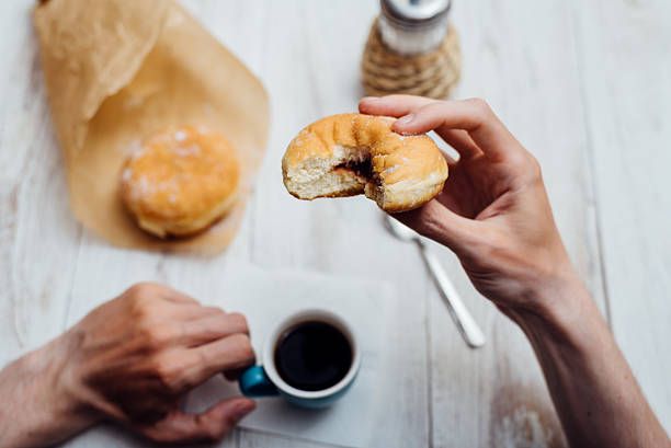 istock Man hands eating Bismarck donut with coffee on wooden table 579222328