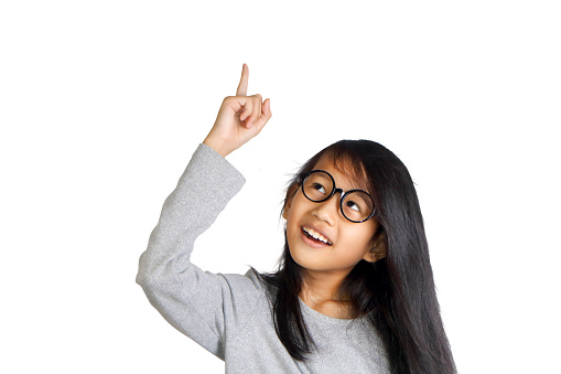 Portrait of beautiful little Asian student girl smiling and raise her pointing finger up get an idea gesture, isolated on white