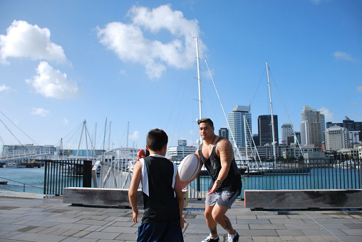 A Pacific Island Man and Boy Playing Rugby against an Urban Auckland Scene, New Zealand
