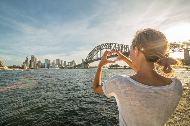 Young woman makes heart shape finger frame on Sydney skyline